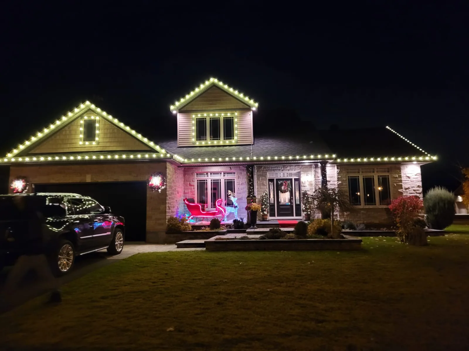 Ranch-style home lit with warm white roofline lighting, wreaths and a lit front walkway